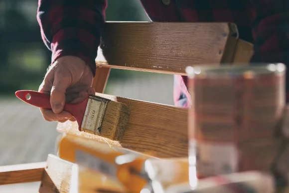 Person streicht Holzbank mit Pinsel